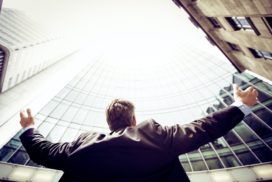 Person with arms stretched out to the side looking up at the sky in front of a building, career values