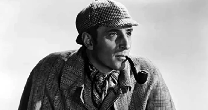 A black and white photo of a portrayal of Sherlock Holmes, with classic cap and pipe