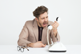 a man in a beige suit yelling into a telephone receiver