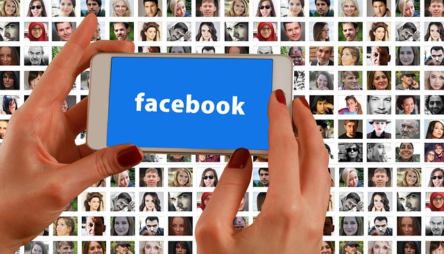 hands holding a smartphone with the facebook logo over a background grid of peoples' faces on screens