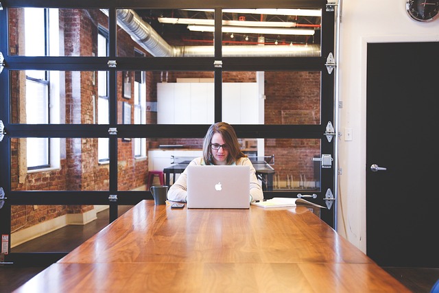 a person sitting alone at a big conference table typing on a laptop