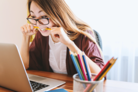 a woman sitting at a computer and biting her pencil