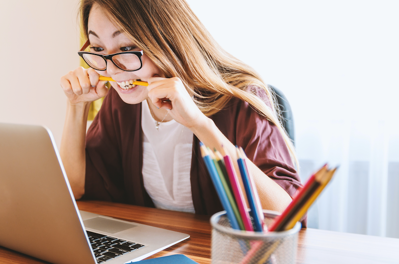 a woman sitting at a computer and biting her pencil