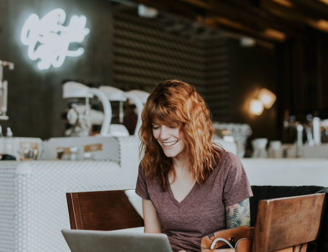 a woman smiling looking at her laptop screen in a cafe