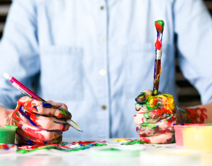 a person in a clean button-down shirt holding very messy colorful paintbrushes